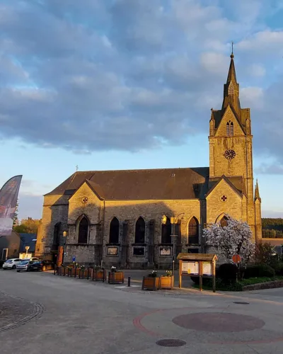 Vue de l’église Saint-Hubert de Redu depuis la place du village, entourée de bâtiments ardennais et baignée par une lumière de fin de journée